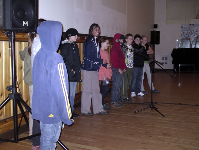 Students giving a presentation, standing around  a woman talking on a microphone.
