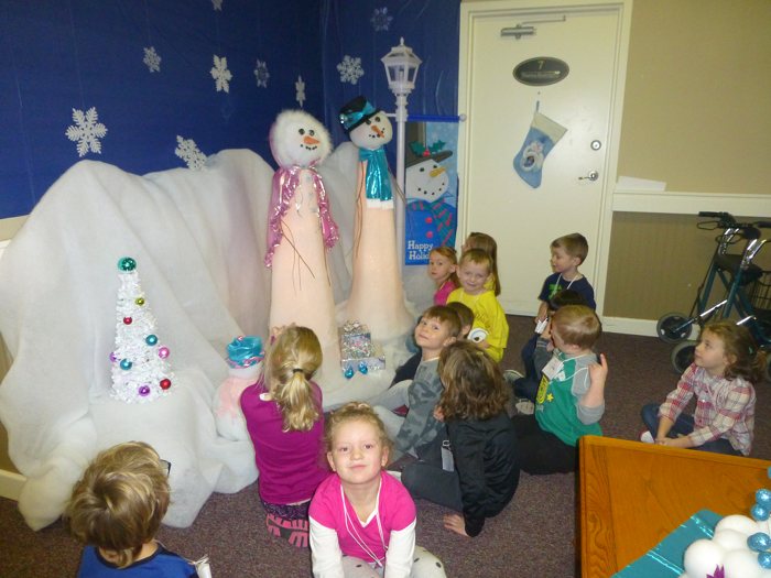 Children sitting on the floor in a room decorated with snowmen and snowflakes.