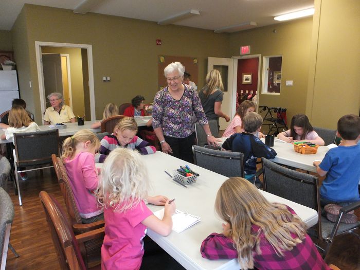 Children working at a table being observed by an elderly woman