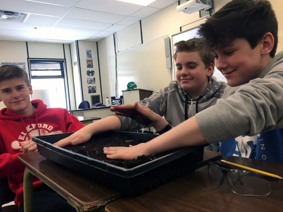 3 boys putting their hands in soil in a classroom. 