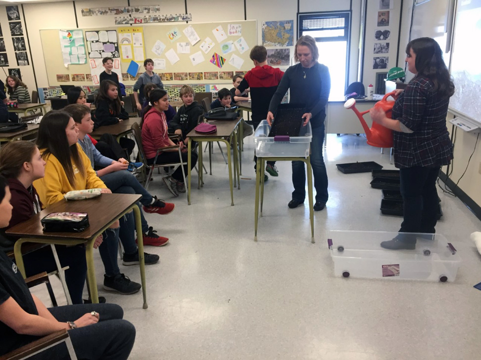 Students  in a classroom observing a teacher with the soil in